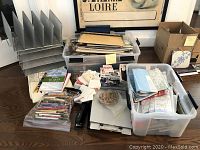 Overall view of wire mesh file holders, clipboards, plastic bins with maps and papers, a stapler, and playing card decks arranged on floor.