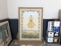Full view of large framed art depicting a golden-dressed figure outdoors, with ornate border and frame.