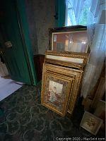 Group of several gold-tone frames stacked against wall under window