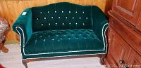 Full view of green velvet love seat with crystal stud detailing and wooden legs.