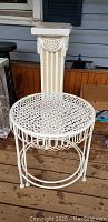 Photo showing one round white wrought iron table with lattice top in front of a cream and gold striped plaster pillar on wooden porch floor.