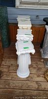 Overview of all four plaster pillar plant stands stacked and aligned on wooden floor, showing their white fluted shafts and classical capitals.