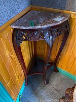 Full view of triangular marble top corner table with curved legs against wood-paneled walls and carpeted floor.