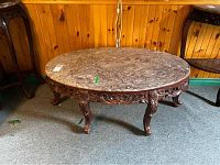 Full front angle view of oval coffee table with marble top and ornate wooden legs.