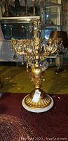 Full view of the gold tone ornate pillar candle stand showing the white marble base and hanging crystal drops
