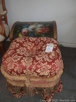 View of floral painted chest behind a red and gold brocade ottoman