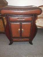 Front view of the storage chest showing two drawers and two doors with metal handles, padded leather-like finish, and nailhead trim.