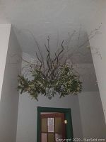 Hanging decorative glass vase with artificial greenery and twig branches from below near hallway door.