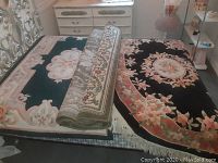 Three carpets on bed: two laid flat side by side and one rolled on top