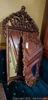 Two ornate mirrors stacked leaning against furniture, showing carved wooden frames and reflective glass surfaces.