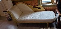 Full side view of the gold and ivory chaise lounge with fabric upholstery and carved wood frame.