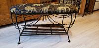 Full view of padded wrought iron bench showing twisted iron legs, lower shelf, and animal print upholstery