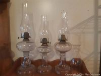 Front view of three clear glass oil lamps with chimneys lined up from tallest to shortest