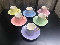 Front view of all six multicolored mini cups with matching saucers arranged on black surface.