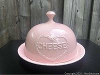 Front view showing dome with embossed heart and CHEESE lettering on pink ceramic plate.