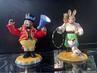 Two Royal Doulton Bunnykins Circus figurines displayed together on a reflective surface, showing their size and detail.