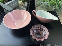 Three bubblegum pink serving pieces on black surface: large ceramic bowl, vintage ceramic gravy boat, vintage glass bowl with frosted rim.