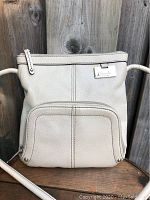 Front view of cream Tignanello leather purse with visible pebbled texture, front pocket, and metal brand plate.