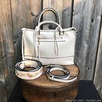 White purse with handles and two extra straps, displayed on wooden surface in natural light.