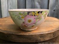 Side view of small Wedgwood ceramic bowl with blush rose and leaf floral exterior design on a wooden surface