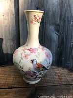 Clear front angle showing bird and floral detailed painting on cream ceramic bud vase.