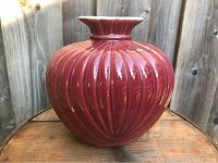 Front view of a large vintage Canadian art pottery vase in a deep red glaze with vertical ribbing and a fluted wavy rim.