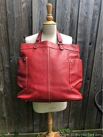 Front view of red Latico leather satchel purse with two large snap-closure exterior pockets, double handles, displayed on mannequin.