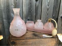 5-piece vintage pink frosted glass vanity set and vase displayed on wood surface against wood fence, showcasing frosted Lily of the Valley floral details