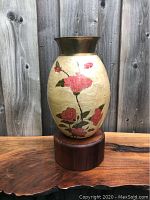 Front view of vase showing pink floral enamel design and brass mouth with wooden base.