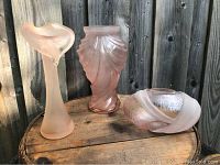 Three pink frosted glass vases placed together on wooden surface with fence background