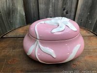 Front view of pink porcelain covered tray with white floral relief design on base and lid.