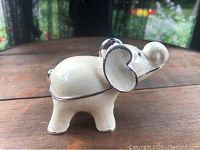 Side angled photo of cream enamel miniature elephant trinket box with silver-tone accents.