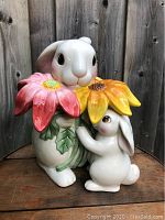 Front view of the large ceramic cookie jar showing two white bunnies, one larger with a pink flower and one smaller with a yellow flower.