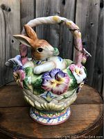 Front view showing bunny inside basket with colorful pansy flowers and twisted handle.