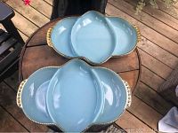 Two blue divided serving trays with gold beaded rims on a round wooden table. One tray shows wear on gold rim, the other in excellent condition