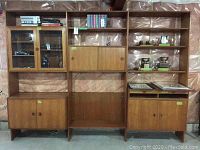 Full view of assembled modular teak wall unit against plastic-covered basement wall