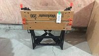 Front view of folded Black & Decker Workmate 200 workbench showing wooden top with printed logo and red clamps.