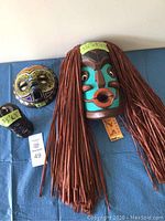 Three pieces: one large painted mask with brown strands, one medium painted mask with yellow and black patterns, and one small black decorative piece