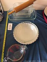 Set of glass baking dishes and pie plates with wooden rolling pin on top, on blue background