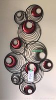 Large metal wall art with concentric circles and multiple red and silver metal candle holders mounted on wall