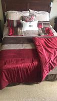 Queen size bed set up on bed showing bedspread, sheets, pillows, and bedskirt in red, beige, brown tones