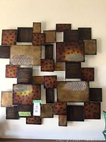 Full view of one metal wall art piece showing overlapping geometric shapes with painted leaf and dotted patterns in warm earthy tones.
