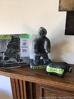 Three pieces of Inuit art shown together on a wooden surface with size labels attached.