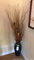 Full view of 67-inch tall dark wicker woven vase with natural twig and feather decor inside, positioned in a corner.