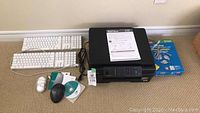 Brother all-in-one printer with two wired keyboards, two mice, installation CDs and user manual laid out on carpeted floor