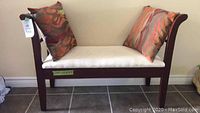 Front and side view of the dark wood hall bench with padded cream cushion and two pillows, shows bench assembled and in good condition.