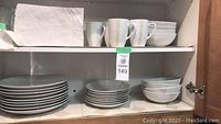 Upper shelf showing stacks of large dinner plates, smaller plates, and bowls in white porcelain with a subtle vertical line design.