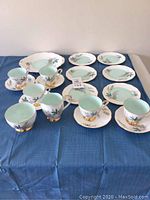 Full spread of the Louise Queen Anne bone china tea set on blue cloth including cups, saucers, dessert plates, cream jug, sugar bowl, and small serving platter