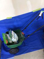 Full view of the Scotts spreader containing two bags of seed and fertilizer against a blue backdrop.