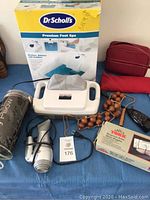 Foot spa box with Dr. Scholl's Premium Foot Spa and Pro-Shiatsu massager shown on table alongside other spa accessories such as wooden bead massage, hand-held massager, and pillow case.